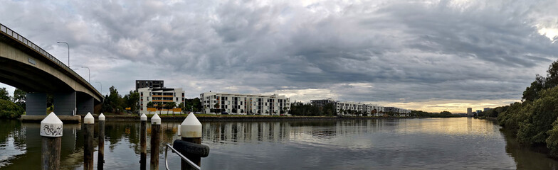 Beautiful panoramic view of a river with reflections of bridge, modern apartment buildings, cloudy sky and trees on water, Parramatta river, Wilson Park, Sydney, New South Wales, Australia
