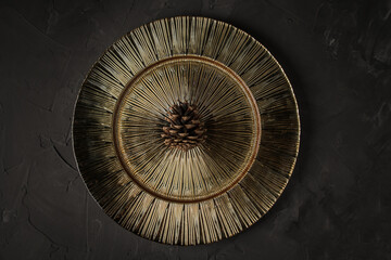 Pine cone on a beautiful gold platter, on a black stone table.