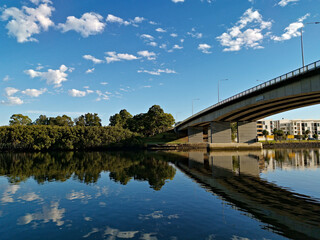 Beautiful view of a river with reflections of bridge, modern apartment buildings, blue sky and trees on water, Parramatta river, Wilson Park, Silverwater, Sydney, New South Wales, Australia
