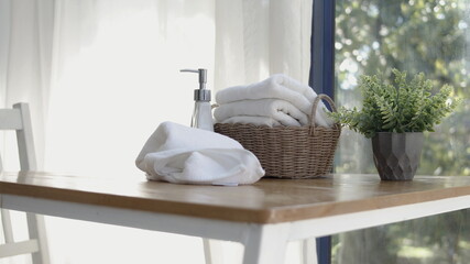 Towel placed on basket, white table top, bottle of liquid soap, spa set for bathing in the bathroom, copy space, bathroom window.