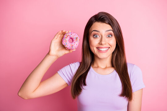 Photo portrait of happy girl holding donut in one hand isolated on pastel pink colored background