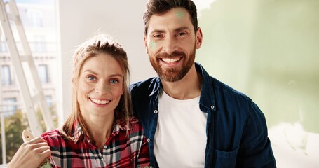 Camera approaching happy young Caucasian couple man and woman hugging while standing in empty apartment near big window during home repair process and smiling to camera. Love concept. Close up