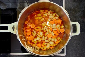 Cooking large beans and sliced carrots with tomato juice in a pressure cooker. Top view, shallow depth of field