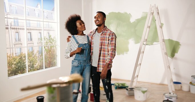 Happy young African American couple stands in room in new own apartment discussing design and decor of house. Wife talking to husband about home repair. Renovation and improving apartment concept
