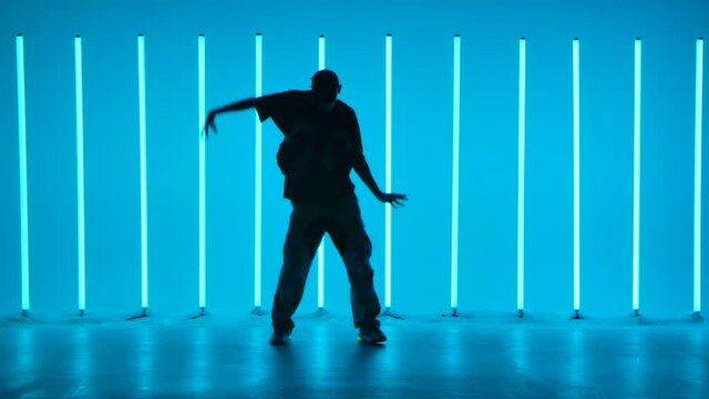 Cool young guy breakdancer dancing hip hop in colorful background with neon lamps. Breakdancing school poster. Silhouette. Slow motion.