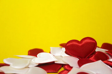 Small red and white hearts that lie in a pile on a yellow background.