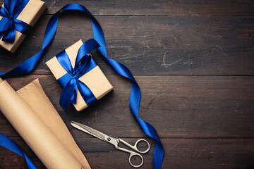 Fototapeta na wymiar box wrapped in brown paper and tied with a blue silk ribbon with a bow, gift on a brown wooden background