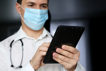 Man doctor in a medical mask with a tablet PC in hands. Work of medical staff during the covid-19 coronavirus epidemic