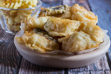 Cod in fried batter with fried potatoes on wooden background. Selective focus.