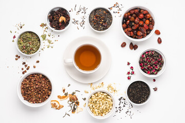 Cup of tea surrounded Different types of tea in bowl on white background. Rose hips, jasmine, rose flower, green, berry, hibiscus tea