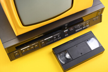 Old yellow vintage TV with VCR and videotape on a yellow background from the 1980s, 1990s, 2000s.