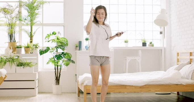 excited young woman holding mobile phone singing and dancing at home