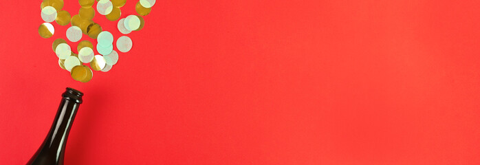 champagne christmas bottle with confetti on red background. Concept holiday atmosphere, new year, celebration, greeting card. Flatlay, top view, frame, copyspace, banner