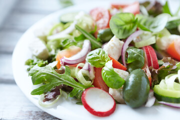 Salad with feta cheese, radish, rocket, green olives, tomatoes, cucumber and fresh basil. Bright wooden background. Close up. 
