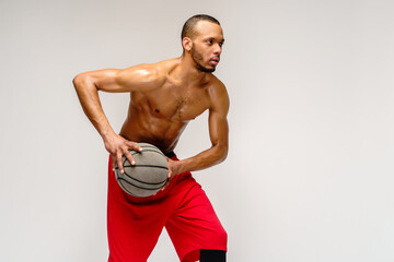 Fototapeta na wymiar Muscular african american sportsman playing basketball shitless over light grey background