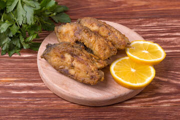 Pieces of fried carp on a wooden board with herbs and lemon