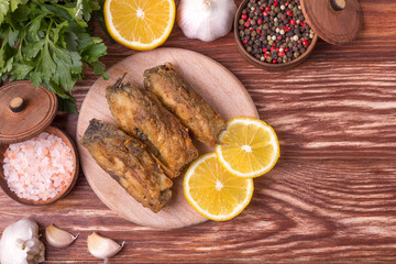 Pieces of fried carp on a wooden board with herbs, spices and lemon. Top view