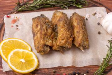 Pieces of fried carp on a wooden board with herbs, spices and lemon. Top view