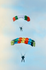 two skydivers on brightly colored parachutes soar above each other high in the blue sky	