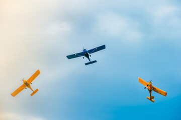 three  small two-pilot airplanes boldly making turns in the blue cloudy sky	