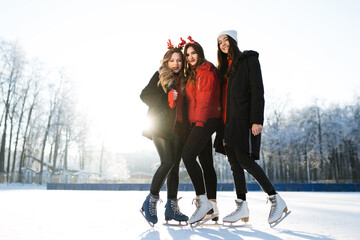 Fototapeta na wymiar Beautiful girlfriends in jackets and headbands in the form of deer antlers skate in winter
