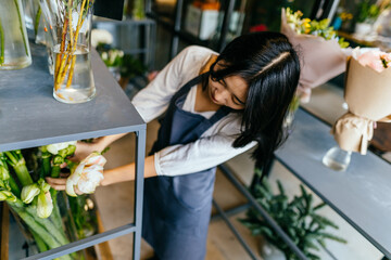 Florist takes amarillis flowers at the fridge. Flower seller in grey apron uniform chooses flowers for future bouquet. Small business concept.