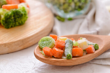 Frozen vegetables in spoon on light background