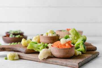 Frozen vegetables in bowls on light background