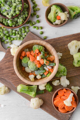 Frozen vegetables in bowls on light background