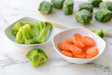 Frozen vegetables in bowls on light background