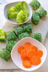 Frozen vegetables in bowls on light background