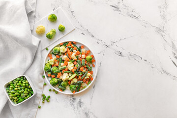 Frozen vegetables in bowls on light background