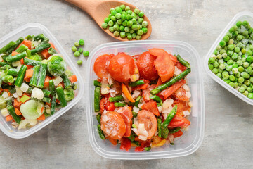 Frozen vegetables in plastic containers on light background