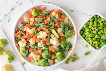 Frozen vegetables in bowls on light background