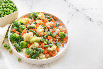 Frozen vegetables in bowls on light background
