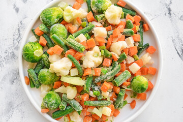 Frozen vegetables in bowl on light background