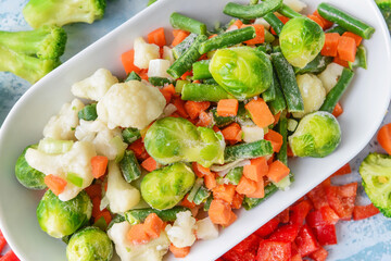 Frozen vegetables in bowl on light background