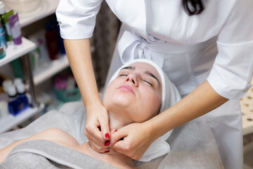 A young beautiful girl lies on the beautician's table and receives procedures, a light facial massage using oil. Woman takes care of herself, enjoys massage