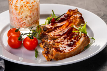 grilled ribs in barbecue sauce with cabbage salad and cherry tomatoes in white plate