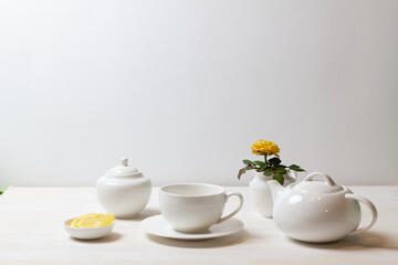 Obraz na płótnie Canvas tea cup with saucer, teapot, sugar bowl, yellow rose in milk jug and lemon on white background ready for drinking