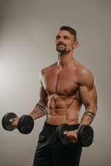 Fototapeta na wymiar A muscular man with a beard is doing bicep curls with dumbbells. An athletic guy is demonstrating his sporty torso. An athlete with tattoos on his forearms is training his arms