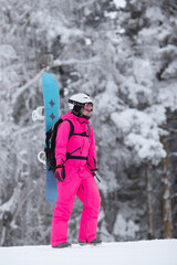 Fototapeta na wymiar Woman in bright pink sportive overall with snowboard on the backpack having fun outisde in snowy day. Winter restorative escape concept. Vertical orientation