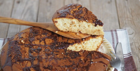 Sliced piece of muffin poured with chocolate icing on a wooden spatula on an ancient wooden background.Homemade healthy food.