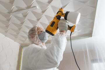 The painter is painting a 3d ceiling with a spray gun.
