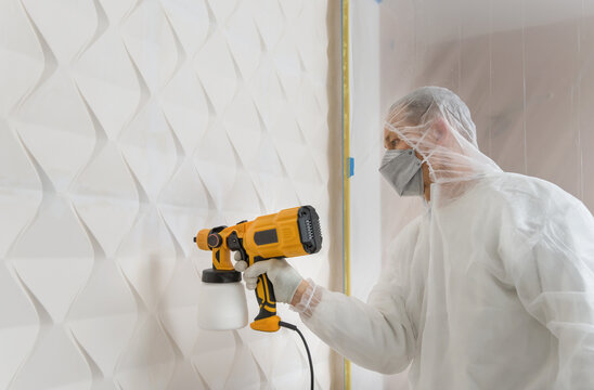 The painter is painting a 3d wall with a spray gun.