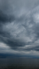 Fototapeta na wymiar Moody dramatic dark contrasting clouds over calm sea. Storm approaching. 