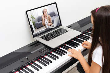 Fototapeta na wymiar A little girl learns to play the piano from video lessons. Online distance learning during covid-19