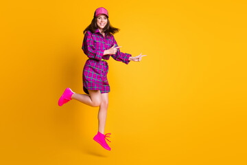 Fototapeta na wymiar Full body portrait of pretty girl jump finger point empty space headwear plaid outfit isolated on yellow color background