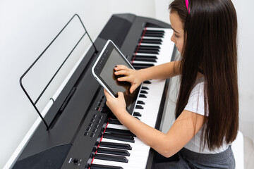 A little girl learns to play the piano from video lessons. Online distance learning during covid-19