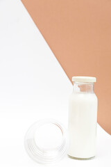 Minimalist still life of milk bottle and glass cup on white and beige background. The concept of ecological and healthy and lifestyle.